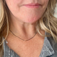 close-up image of female model wearing handmade necklace with 3 tiny 14K yellow gold wire hearts on oxidized sterling silver chain