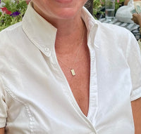 close-up image of model wearing handmade 14K yellow furever dog tag necklace with small birthstone on 14K chain.